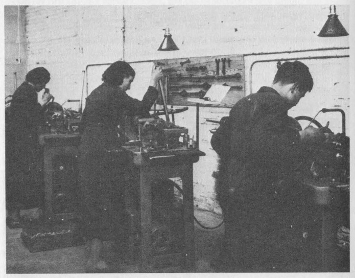 “Spanish men and women working side-by-side in a small, modern machine shop.”