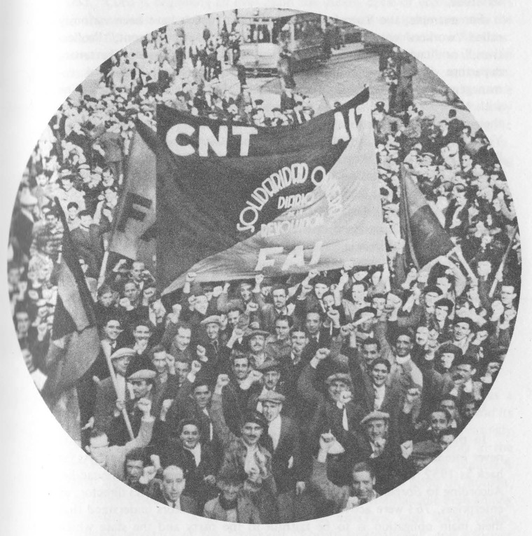 “In a mass demonstration in Barcelona, workers hold a banner reading, ’Solidaridad Obrera, the daily newspaper of the Revolution.’ The banner is inscribed with the initials CNT, FAI, and AIT (the International Workingman’s Association).”