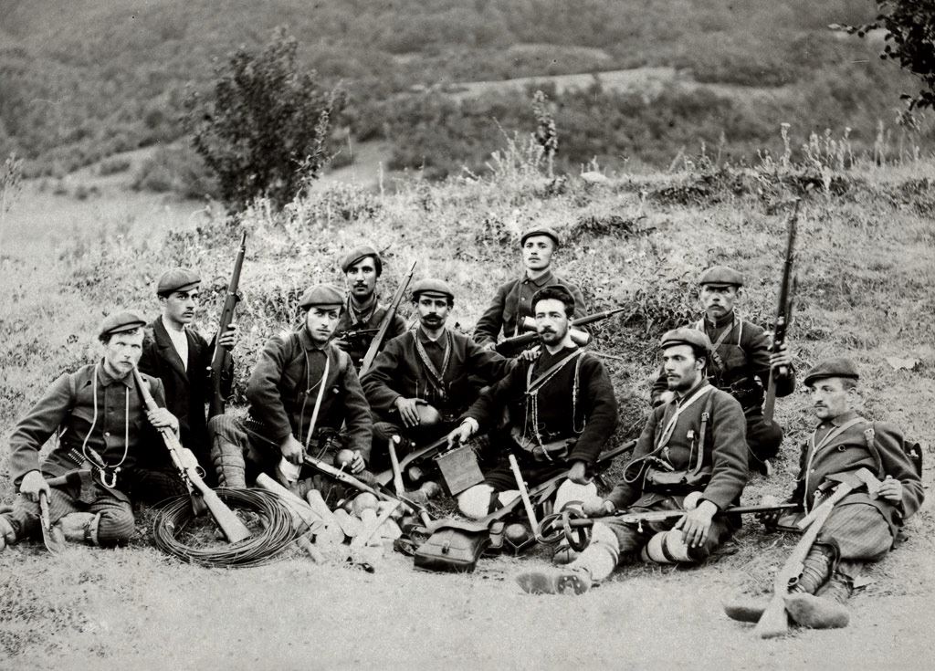 Treća veleška četa – tehničko odeljenje.  Četu je predvodio vojvoda Nikola Dečev (sredina, tamna uniforma; 1880.-1903.), anarhista poreklom iz Bugarske (Stara Zagora) koji je bio deo struje koja je i formalno učestvovala u makedonskoj revolucionarnoj organizaciji. Fotografija datira iz 1903 godine, kratko pre nego što su u bitci sa turskom vojskom kod sela Lukovo u blizini Kratova (istočna Makedonija) većina njih poginuli, uključujući i Dečeva.  Prvi s leva na slici je Julij Cezar Rozental (sekretar čete; poginuo u istoj bitci sa Dečevom), anarhista i poet poljsko-ruskog porekla. Njegov otac, August Rozental,  je bio revolucionar koji je kao organizator jednog ustanka u Ukrajini bio osuđen na smrt, da bi zatim presuda bila zamenjena progonstvom u Sibir. Posle 25 godina sa porodicom uspeva iz Sibira pobeći u Bugarsku gde kao lekar radi po raznim mestima. Obojica su iznimno zaslužni za širenje slobodarskih ideja na ovim prostorima. To naravno nije prošlo neprimećeno od strane vlasti, pa je August Rozental 1889. proteran iz Bugarske u Vranje, gde je i umro.
